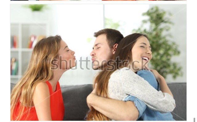 Stock photo of a man hugging his girlfriend while kissing another woman